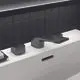 Schwarze Ideal Standard Waschtischarmatur mit eckigen Griffen, montiert auf einer weißen Fläche, hinterlegt mit einer gefliesten schwarzen Wand.